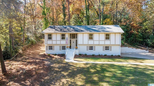 bi-level home with brick siding, a view of trees, and a front lawn