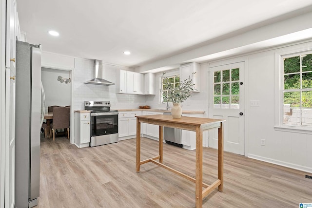 kitchen with backsplash, wall chimney range hood, light wood-type flooring, appliances with stainless steel finishes, and white cabinetry