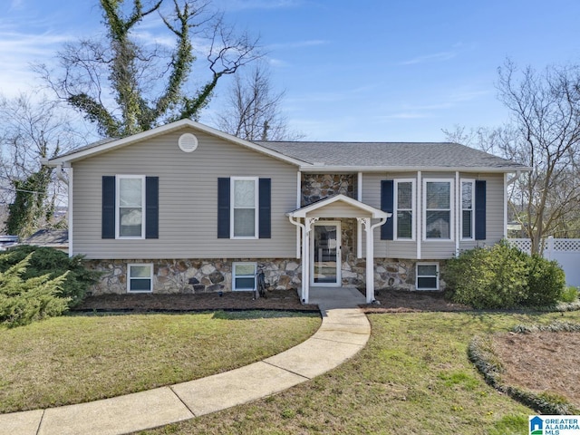 bi-level home with stone siding, fence, a front yard, and roof with shingles