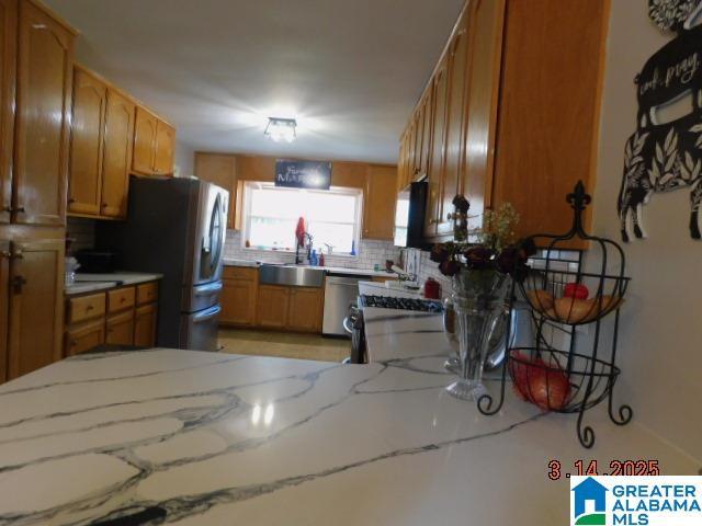 kitchen with brown cabinets, a sink, light stone counters, tasteful backsplash, and stainless steel appliances