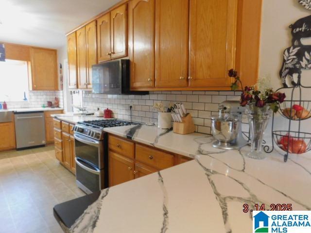 kitchen featuring decorative backsplash, brown cabinetry, light stone countertops, and stainless steel appliances