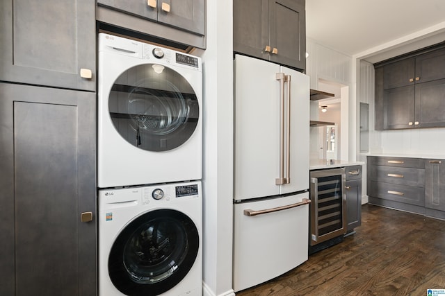 clothes washing area with dark wood finished floors, laundry area, stacked washer and dryer, and beverage cooler