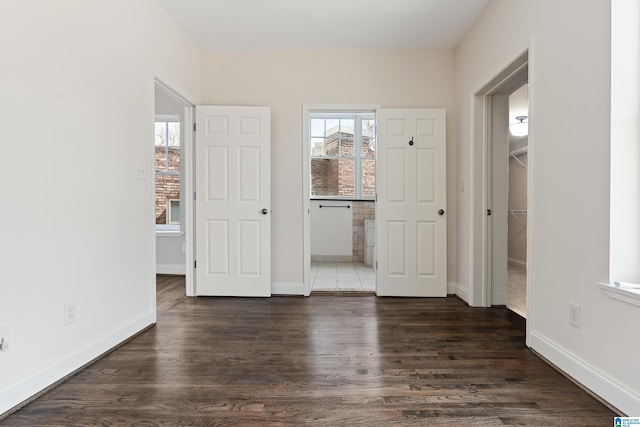 unfurnished bedroom with a walk in closet, dark wood-type flooring, multiple windows, and baseboards