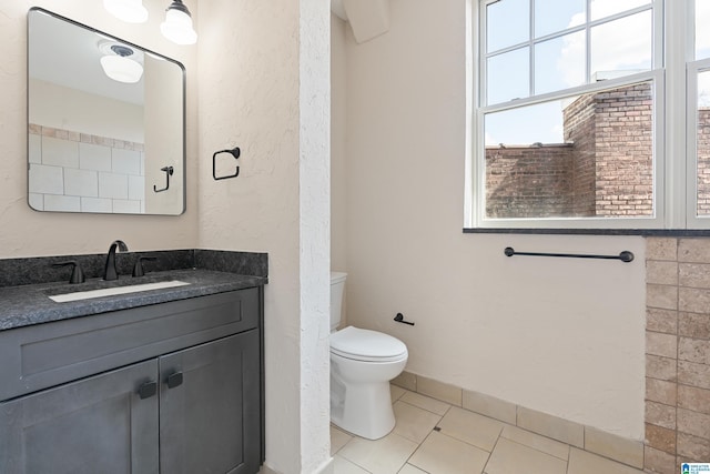 bathroom featuring tile patterned floors, toilet, baseboards, vanity, and a textured wall