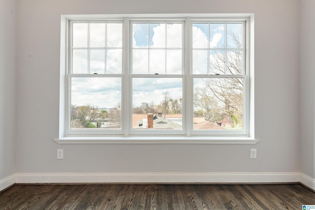 empty room featuring baseboards, plenty of natural light, and dark wood-type flooring