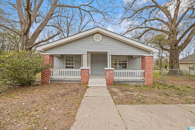 bungalow-style house with a porch, fence, and brick siding