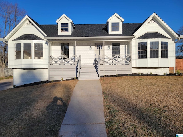 view of front of house featuring brick siding, a porch, a front yard, and roof with shingles