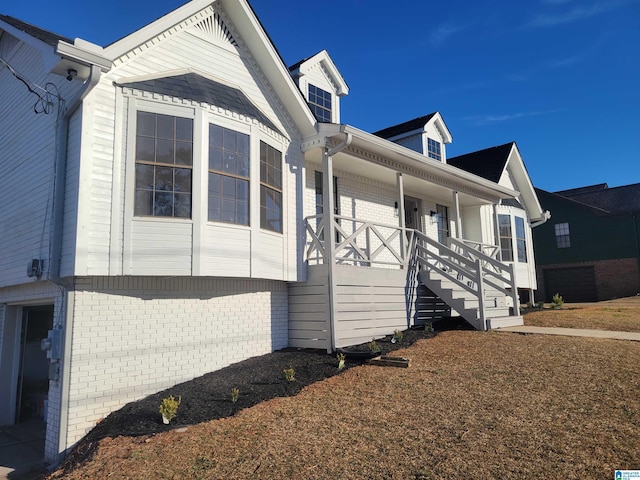 view of property exterior featuring stairway, brick siding, and covered porch