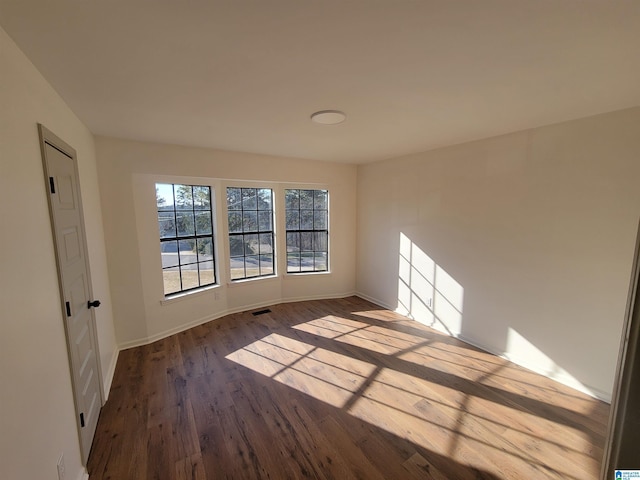 empty room featuring dark wood-type flooring, baseboards, and visible vents