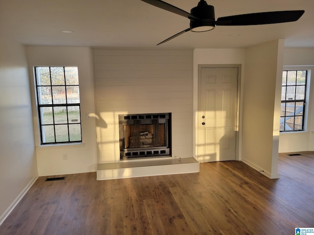 unfurnished living room with visible vents, a fireplace with raised hearth, a ceiling fan, wood finished floors, and baseboards