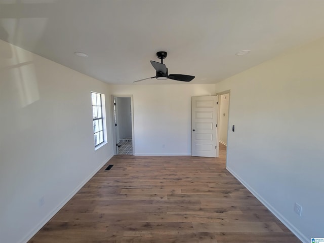 spare room with a ceiling fan, visible vents, wood finished floors, and baseboards