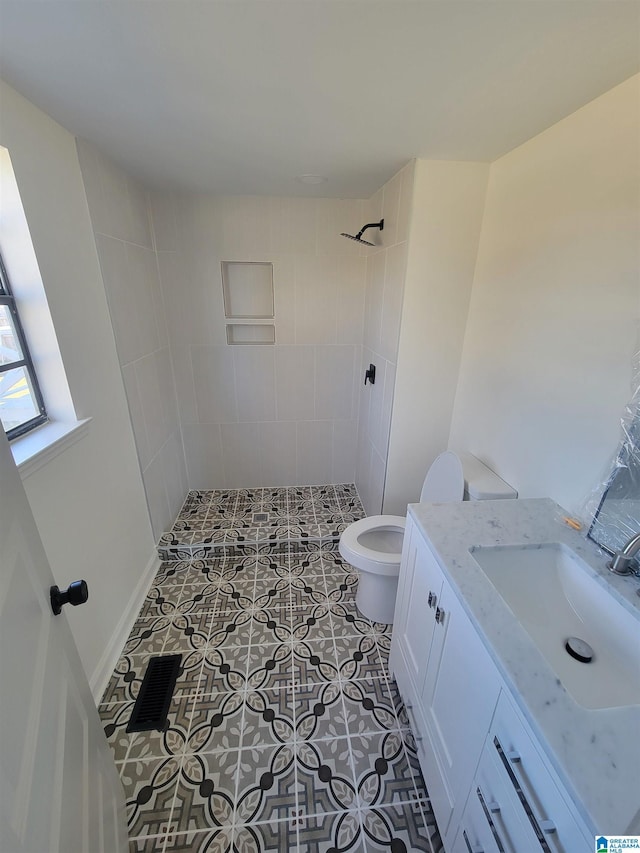 bathroom with vanity, toilet, visible vents, and tiled shower