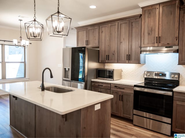 kitchen featuring ornamental molding, under cabinet range hood, a sink, stainless steel appliances, and a chandelier