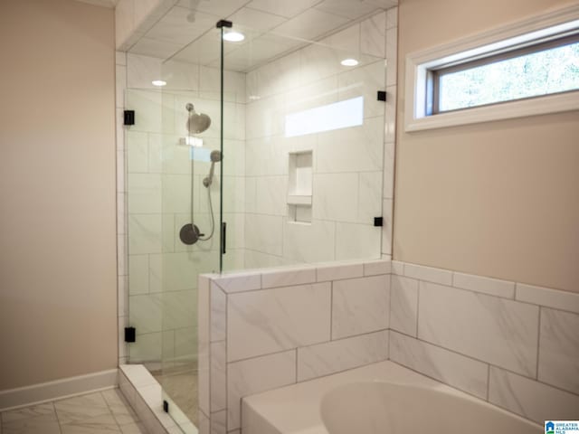 bathroom featuring marble finish floor, baseboards, a shower stall, and a garden tub