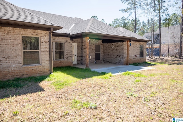 back of house featuring brick siding, a yard, a shingled roof, and a patio
