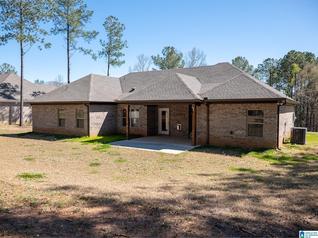rear view of house featuring brick siding, central air condition unit, roof with shingles, a yard, and a patio area
