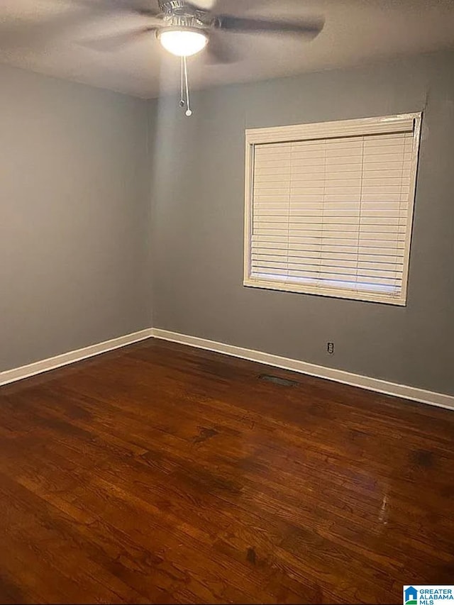 spare room with baseboards, ceiling fan, and dark wood-style flooring