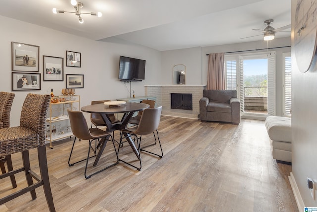 dining room featuring ceiling fan, light wood-style flooring, and a fireplace