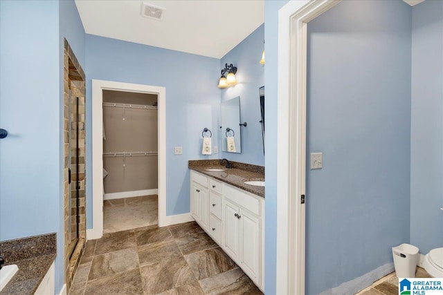 full bath with visible vents, a walk in closet, baseboards, double vanity, and a sink