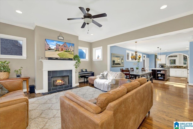 living area featuring ornamental molding, recessed lighting, ceiling fan with notable chandelier, a fireplace, and wood finished floors