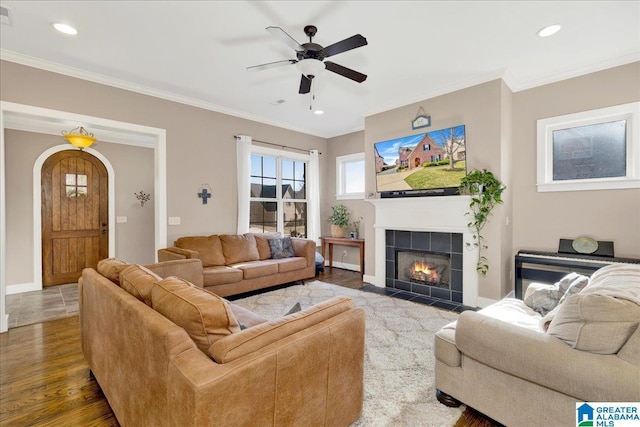 living area featuring wood finished floors, a ceiling fan, a fireplace, arched walkways, and crown molding