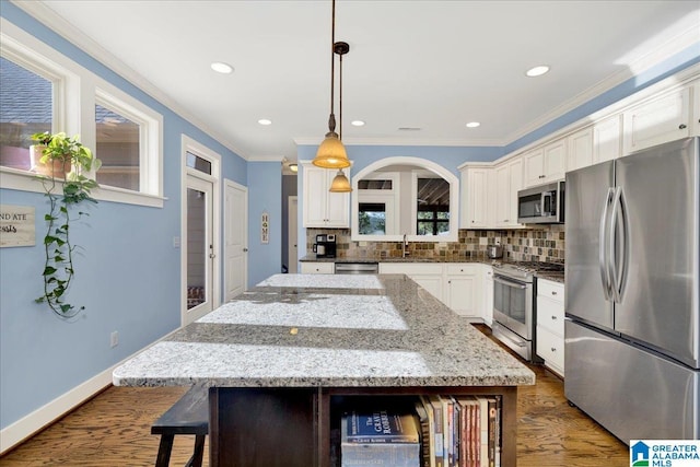 kitchen with tasteful backsplash, a kitchen island, ornamental molding, appliances with stainless steel finishes, and dark wood-style floors