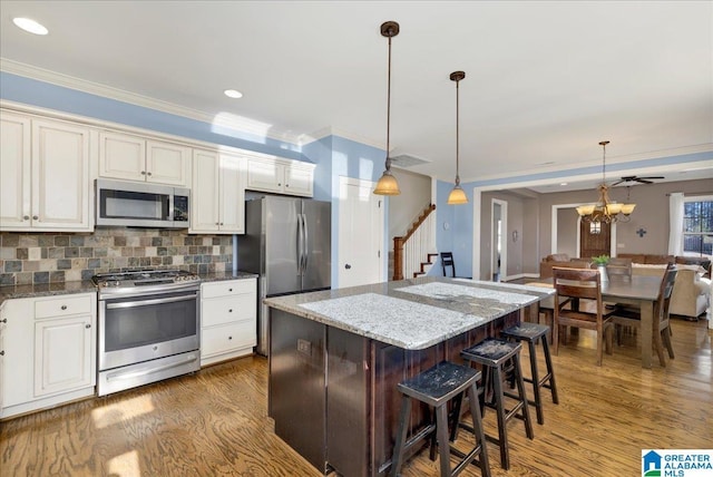 kitchen with wood finished floors, tasteful backsplash, appliances with stainless steel finishes, and ornamental molding