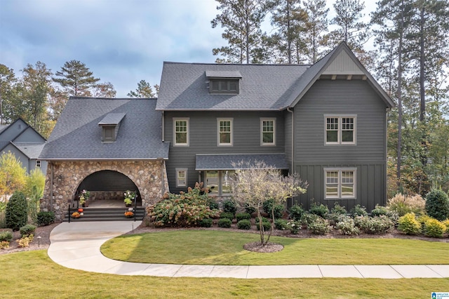 view of front of home featuring stone siding, board and batten siding, a shingled roof, and a front yard
