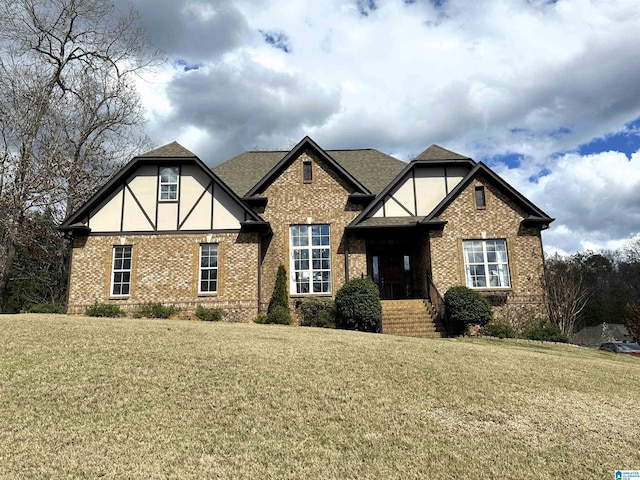 tudor home featuring brick siding, a shingled roof, and a front lawn