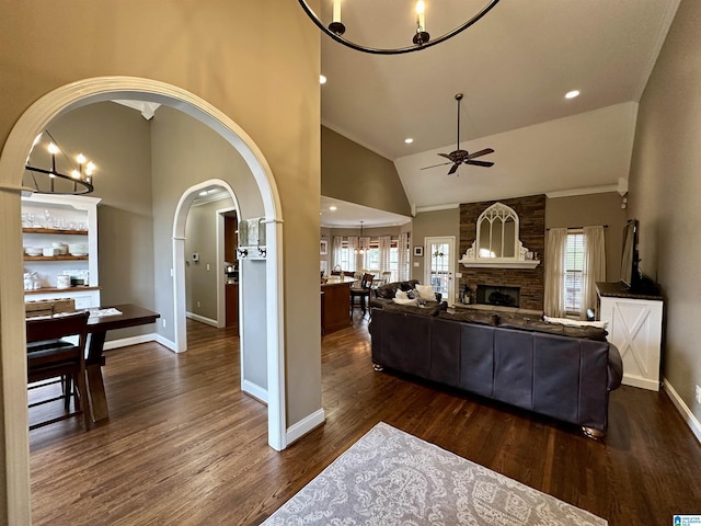 living room with ceiling fan with notable chandelier, baseboards, dark wood finished floors, arched walkways, and a fireplace