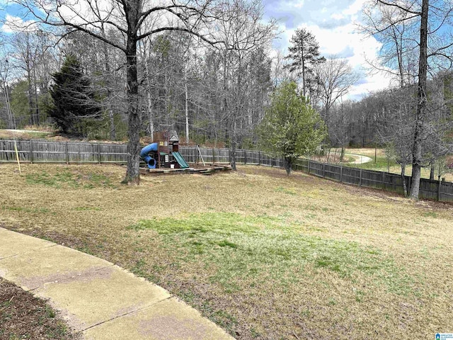 view of yard with a fenced backyard, a playground, and a forest view