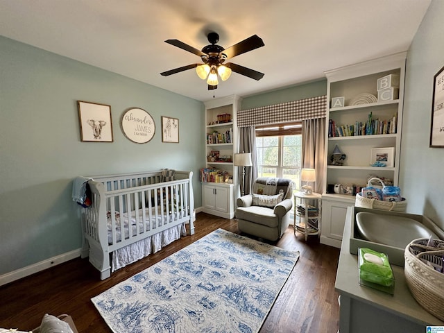 bedroom with a nursery area, baseboards, wood finished floors, and a ceiling fan