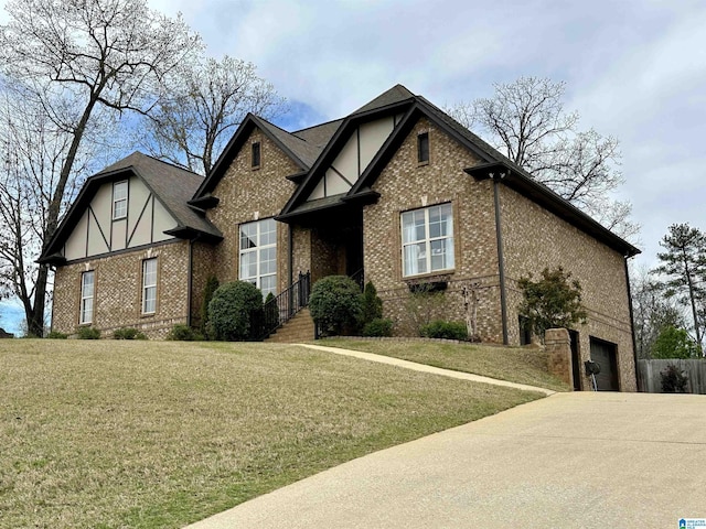 tudor house with a front yard, an attached garage, brick siding, and concrete driveway