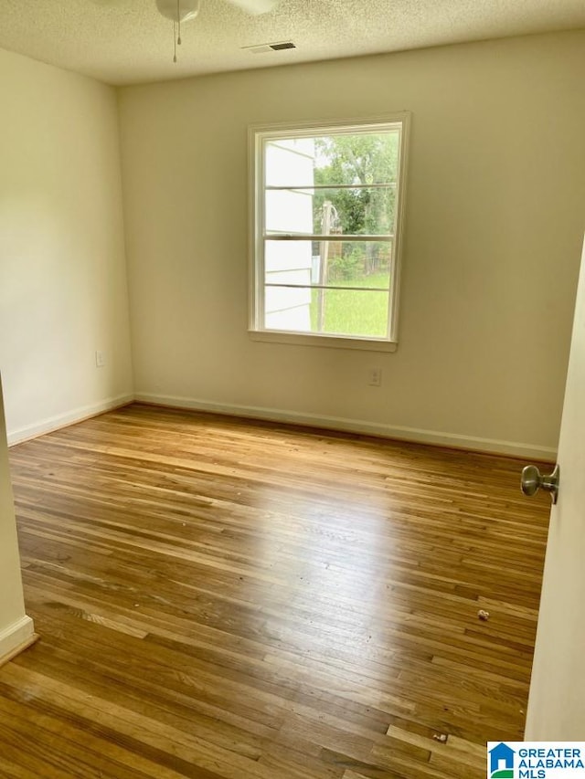 unfurnished room featuring visible vents, a textured ceiling, and wood finished floors