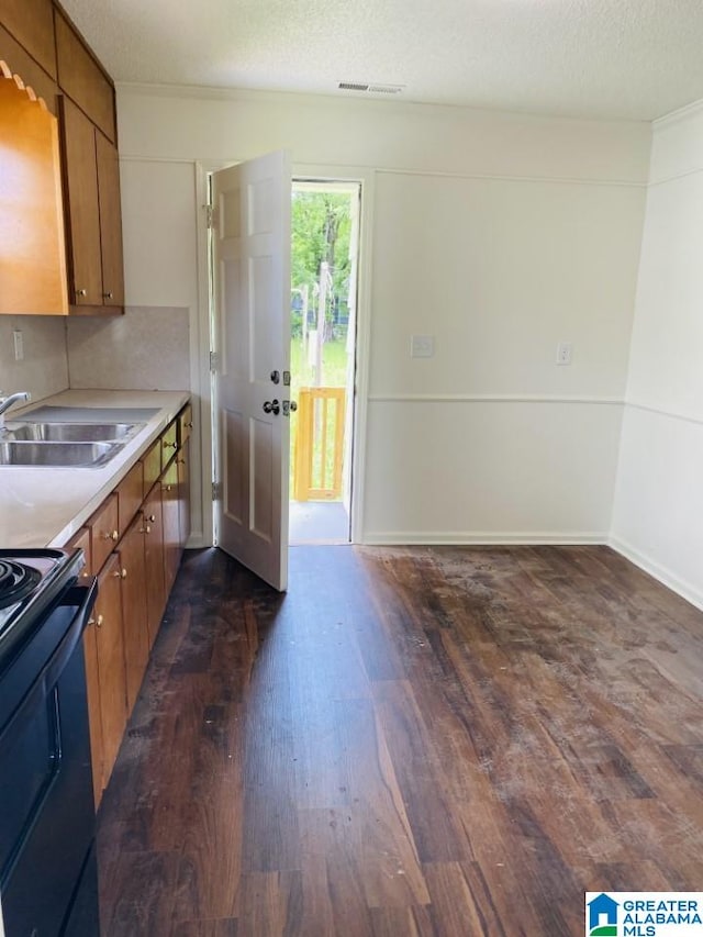 kitchen featuring light countertops, brown cabinets, dark wood-style floors, electric range, and a sink