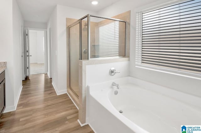 full bath featuring a shower stall, baseboards, wood finished floors, a bath, and vanity