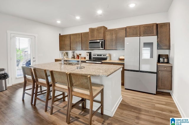 kitchen featuring a kitchen bar, light wood-type flooring, a center island with sink, a sink, and appliances with stainless steel finishes