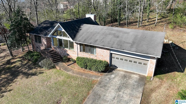 view of front facade with concrete driveway, an attached garage, a shingled roof, brick siding, and a chimney