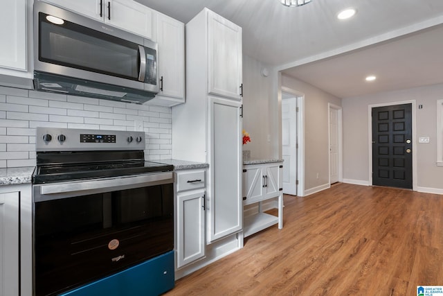 kitchen with backsplash, light stone counters, stainless steel appliances, light wood-style floors, and white cabinetry