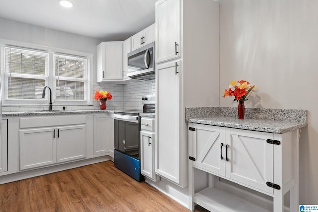 kitchen with tasteful backsplash, stainless steel microwave, electric range oven, light wood-style floors, and white cabinets