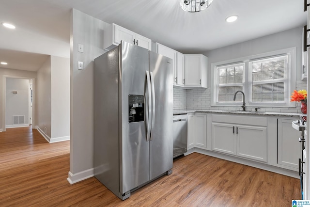 kitchen with light stone counters, decorative backsplash, light wood-style floors, stainless steel appliances, and a sink