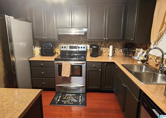 kitchen with under cabinet range hood, a sink, stainless steel appliances, light countertops, and decorative backsplash