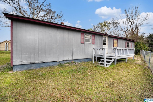 rear view of property featuring a lawn, a wooden deck, and fence