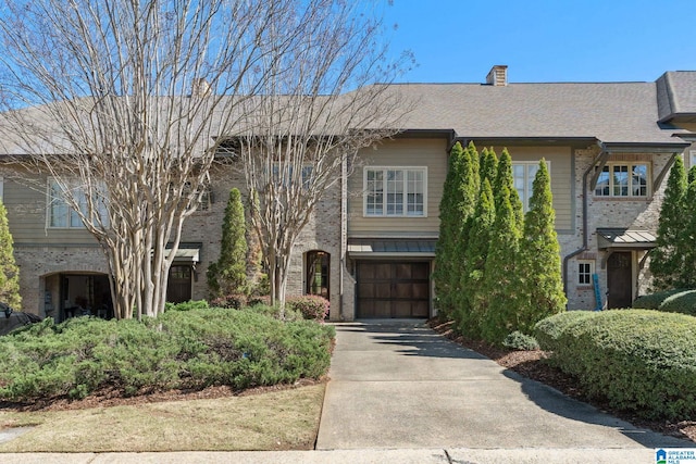 view of front of property featuring brick siding, driveway, a chimney, and a garage