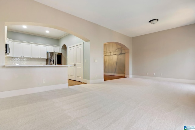 unfurnished living room with arched walkways, recessed lighting, light colored carpet, and baseboards