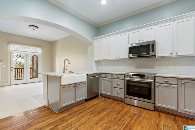 kitchen with gray cabinets, appliances with stainless steel finishes, a peninsula, crown molding, and decorative backsplash