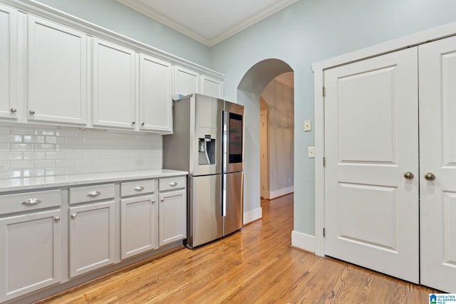 kitchen featuring light wood-type flooring, arched walkways, crown molding, stainless steel fridge, and backsplash
