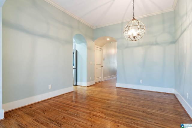 empty room with arched walkways, ornamental molding, baseboards, and wood finished floors