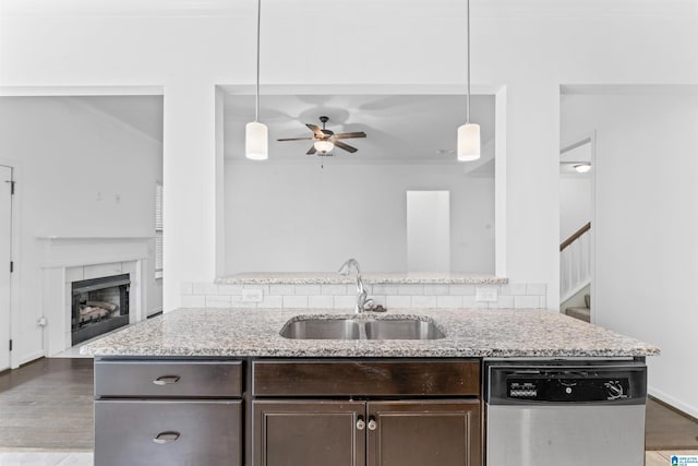 kitchen with light stone countertops, dark brown cabinets, dishwasher, a sink, and a ceiling fan