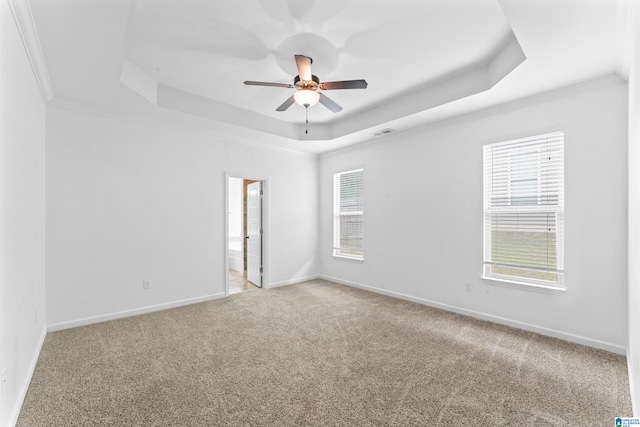 carpeted empty room featuring ceiling fan, a tray ceiling, visible vents, baseboards, and ornamental molding